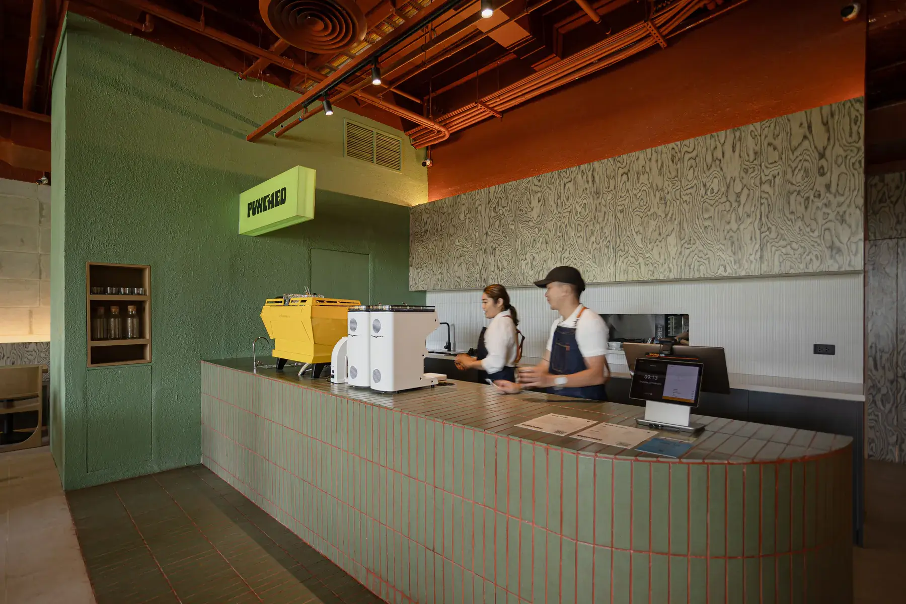 Baristas behind the sage-tiled counter under the lit Punched sign at Mabuhay Tower
