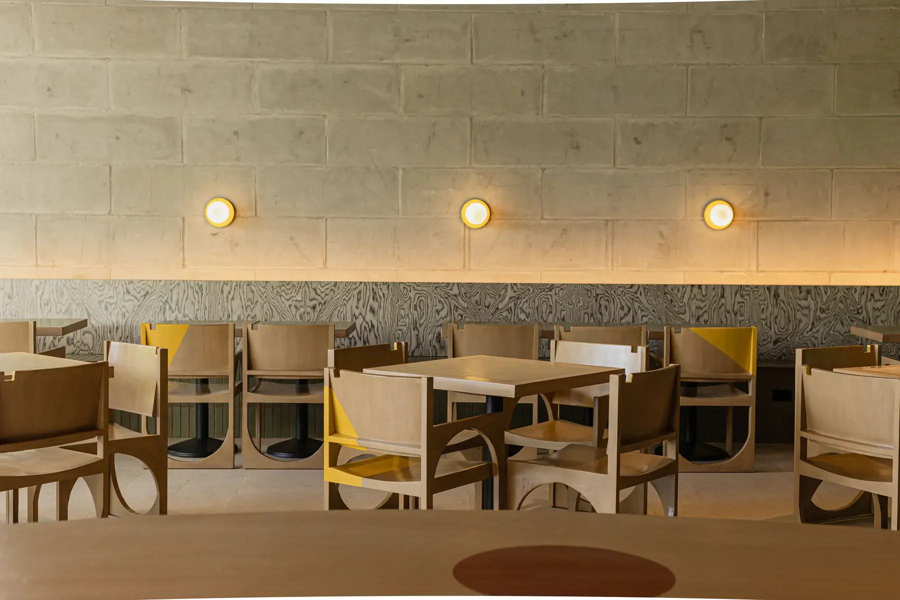 The dining room: timber chairs with yellow accents under warm wall lights