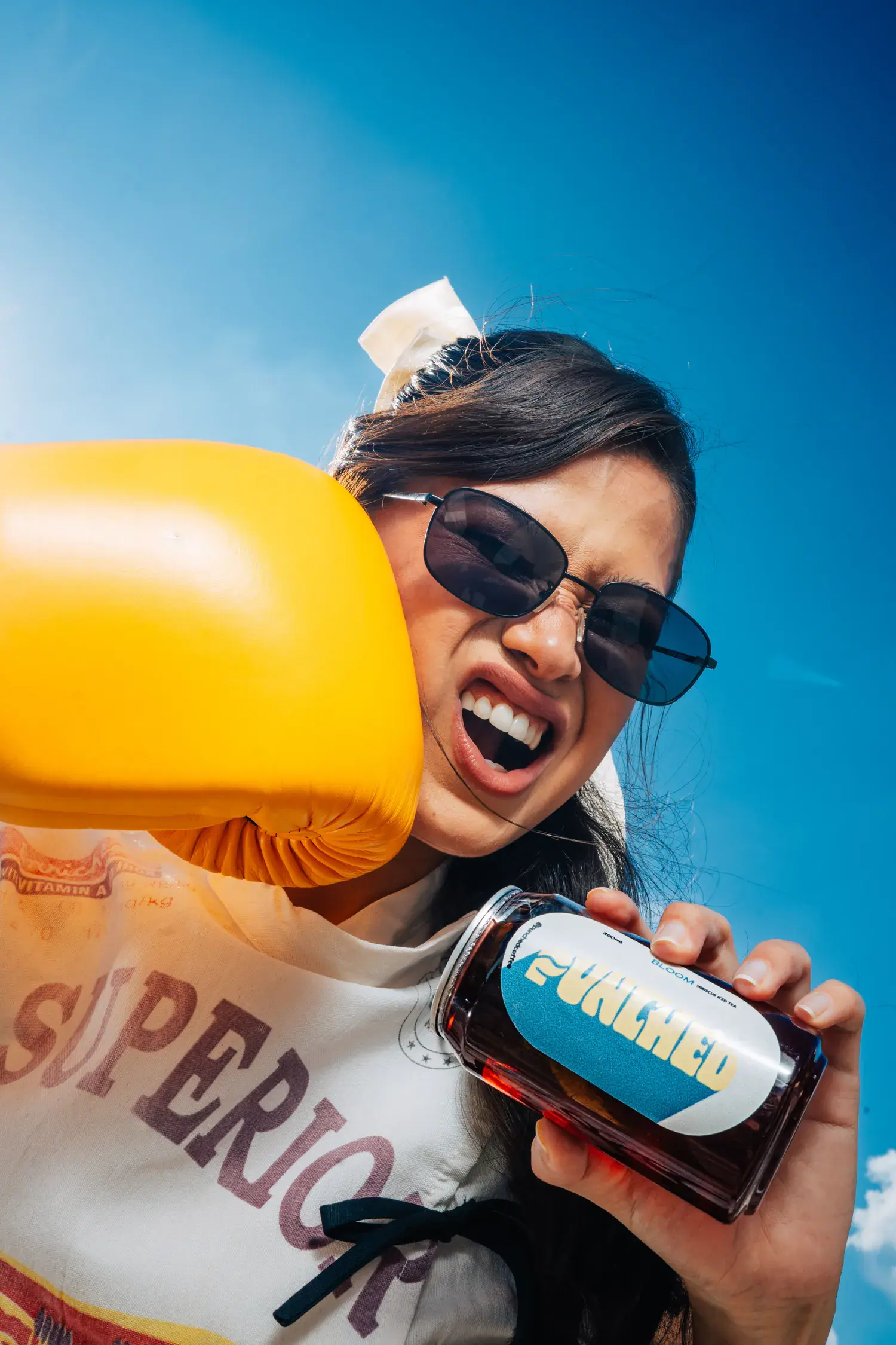 Yellow boxing glove holding up a Punched bottle against blue sky