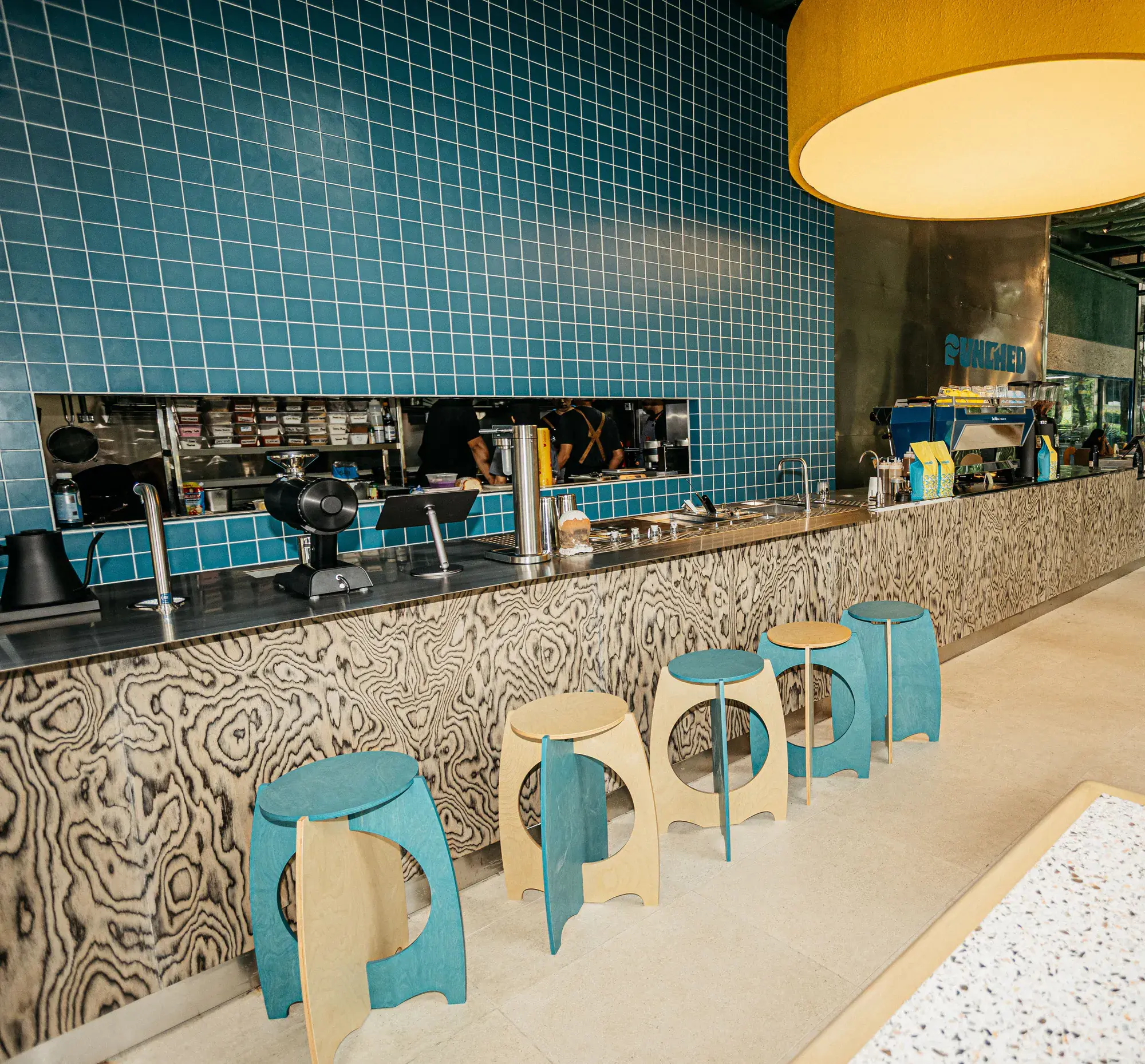 Blue-tiled bar with timber stools under a yellow pendant at Johndorf Tower