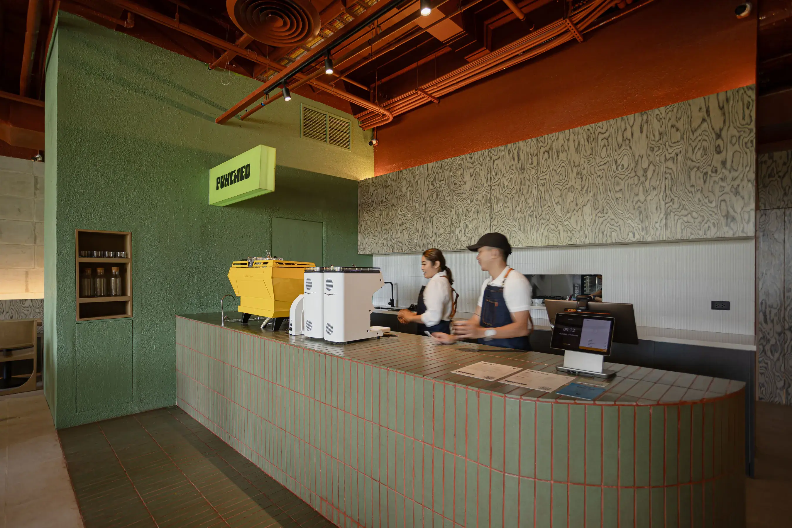 Baristas behind the sage-tiled counter under the lit Punched sign at Mabuhay Tower