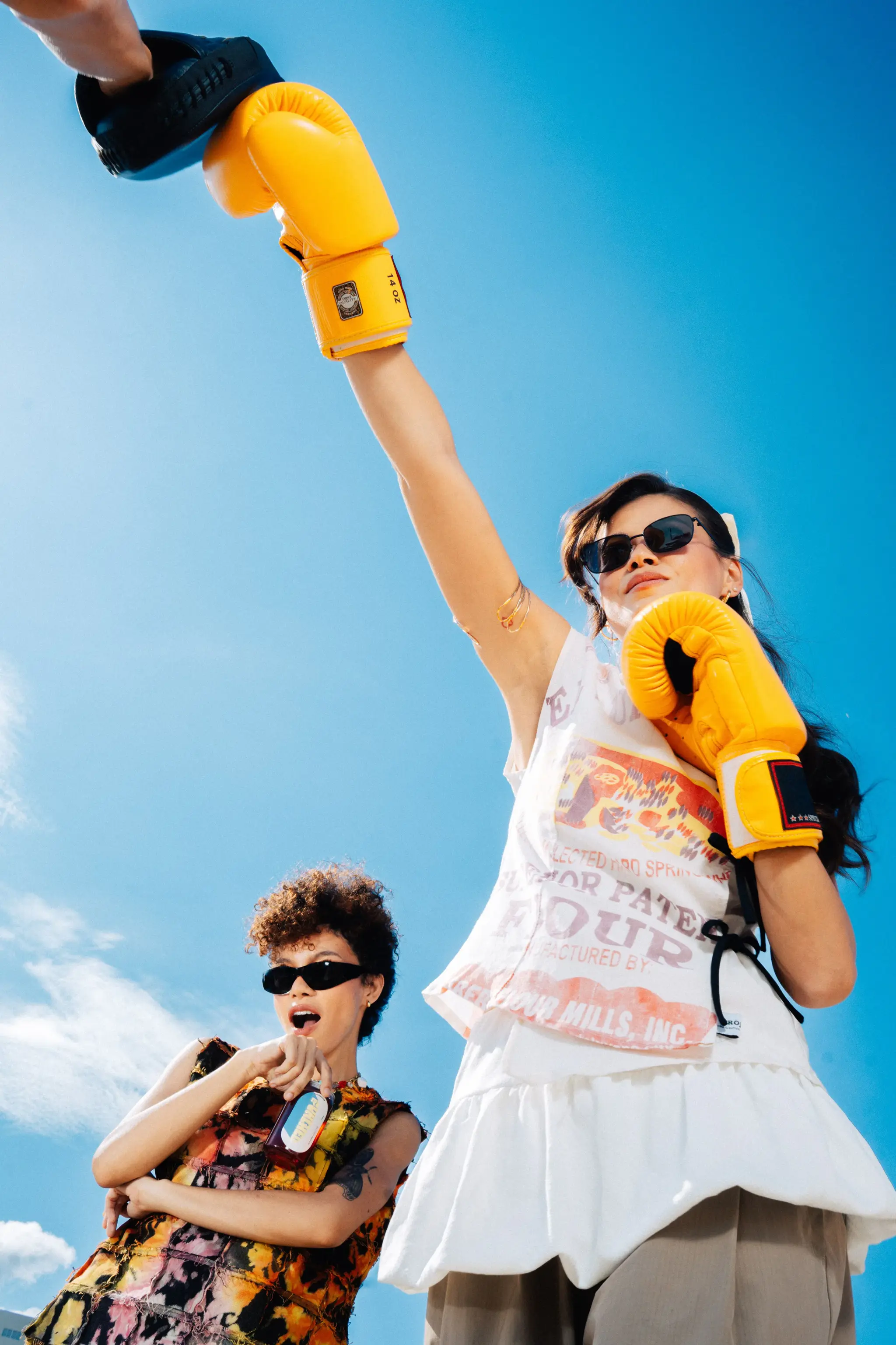 Model raising a yellow boxing glove into a clear blue sky