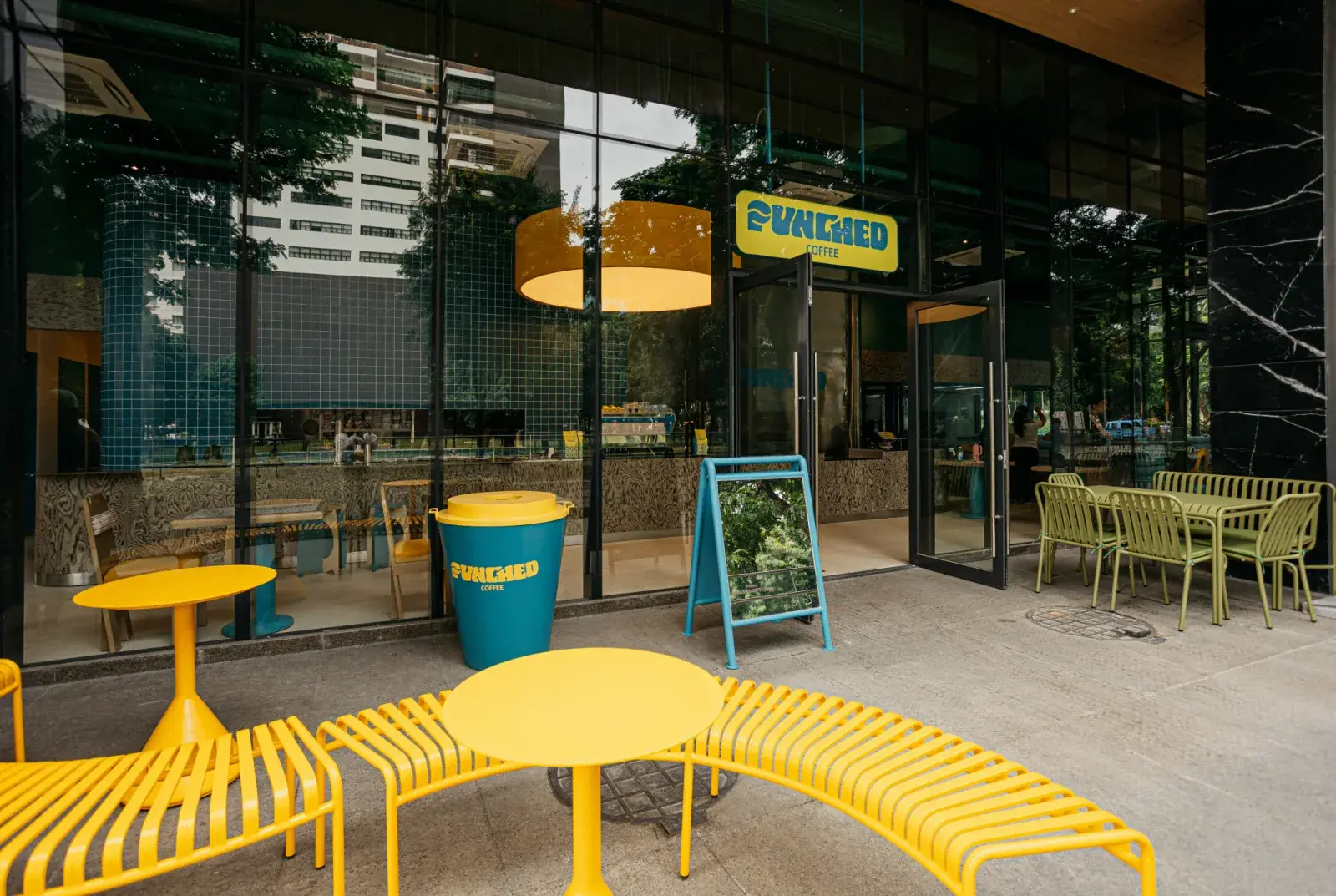 The yellow Punched Coffee sign above the café entrance, with yellow benches and tables on the terrace